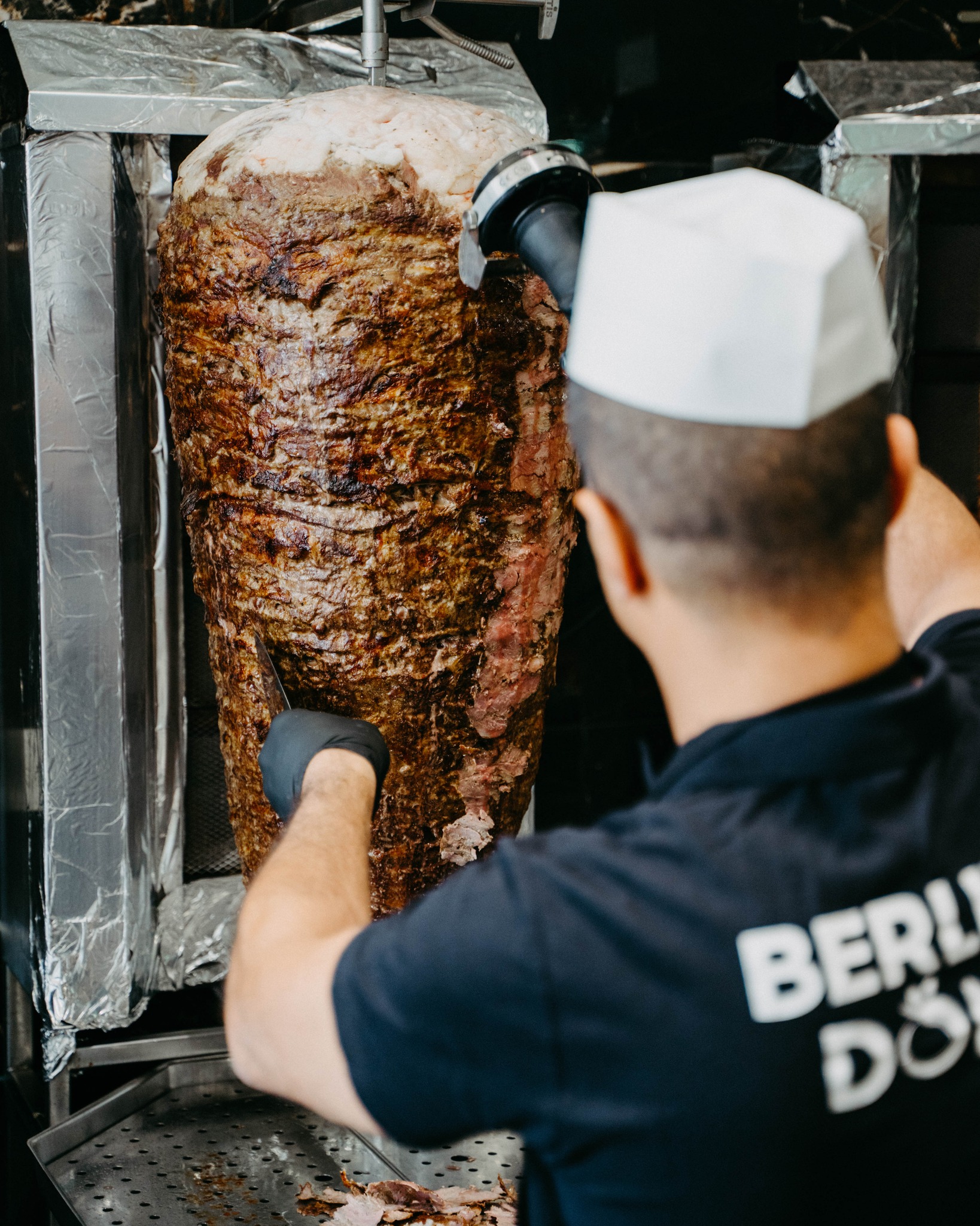 Mitarbeiter schneidet Kalbfleisch vom Spieß